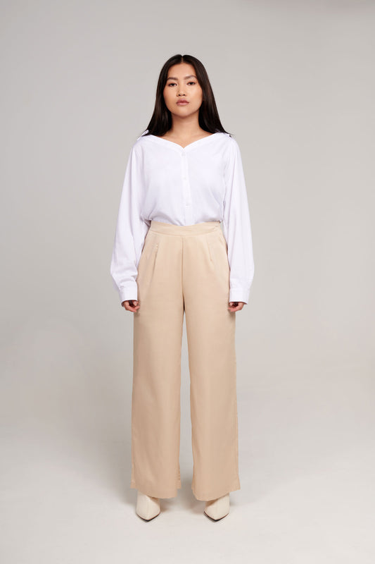 a woman in light beige high-waisted pants with a crossover detail at the front and white open neck button up shirt in an ultra soft sustainable fabric